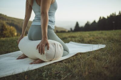Kobieta w legginsach siedzi na wałku na trawie, z widokiem na góry w tle