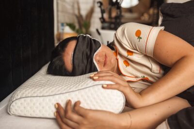 Kobieta w opasce na oczy odpoczywa na białej poduszce ortopedycznej w przytulnym wnętrzu