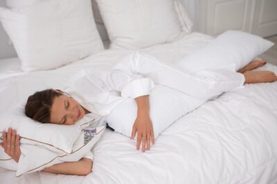 Kobieta leży na łóżku, przytulając poduszki na białej pościeli