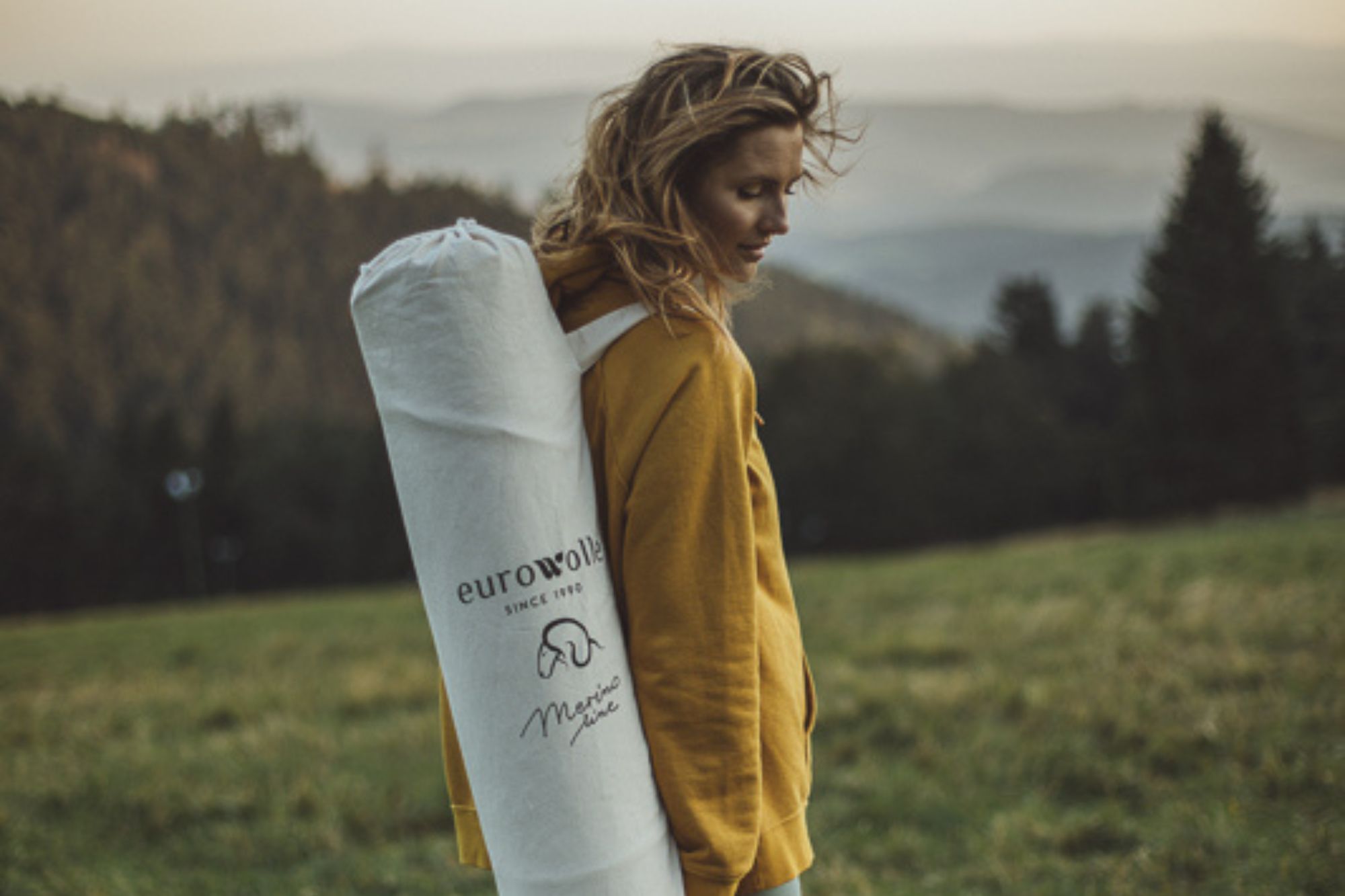 Kobieta w żółtej bluzie z podłużną torbą na plecach w krajobrazie górskim