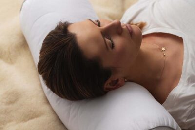 kobieta leży na poduszce w białej koszulce na tle jasnego materiału