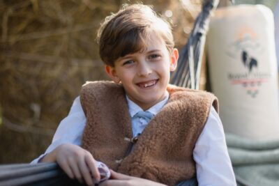 Chłopiec w brązowej kamizelce siedzi w hamaku na tle słomy