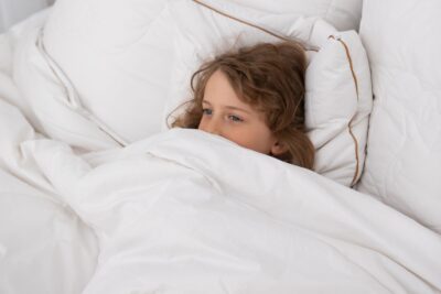 Dziecko leży w łóżku przykryte białą kołdrą, otoczone poduszkami