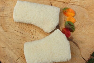 białe mitenki wełniane na tle drewnianego plastra z kolorowymi liśćmi