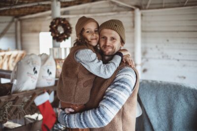Rodzina w wiejskim wnętrzu, ojciec trzyma syna na rękach, oboje uśmiechnięci, w tle dekoracje świąteczne