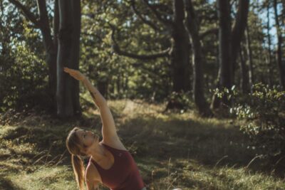 Kobieta wykonująca ćwiczenie jogi w lesie, w tle drzewa i trawa
