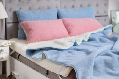 Poduszki w kolorze niebieskim i różowym na łóżku z niebieską kołdrą wełnianą na białym ochraniaczu na materac