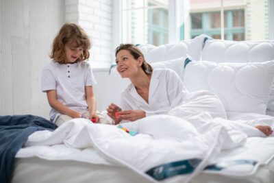 Kobieta i dziecko bawią się w łóżku otoczeni białymi poduszkami i kołdrą