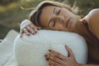 Kobieta leży na poduszce do medytacji w kolorze białym, w naturalnym otoczeniu