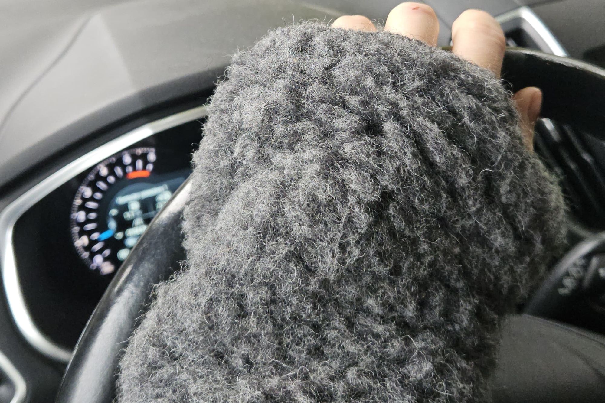 Dłoń w szarej rękawiczce z wełny trzymająca kierownicę samochodu