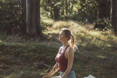 Kobieta medytująca w lesie, na trawie, w sportowym stroju