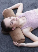 Kobieta leży na szarej wykładzinie z brązowym wałkiem pod szyją